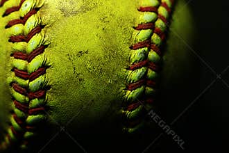 Yellow softball closeup with red seams on black background.