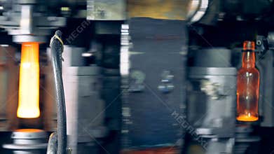 Melted glass mass is being transformed into shaped bottles