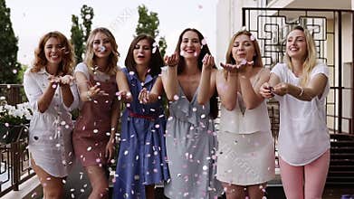 Front view of six attractive caucasian young women playfully blowing bright colored confetti from their hands together