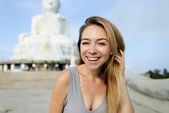 Portrait of blonde female person standing near white concrete statue of Buddha in Phuket.