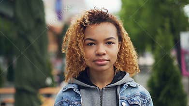 Slowmotion portrait of pretty African American girl modern teenager looking at camera and smiling while standing in