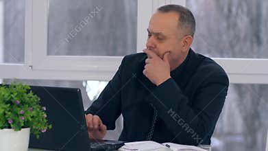 Old businessman work with laptop computer and takes notes in notebook in office