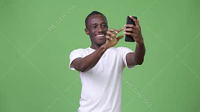 Young African man video calling with phone against green background
