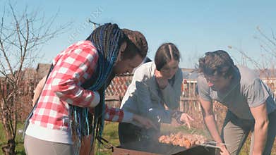 Group of young people friends Barbecue shashlik meat on top of charcoal grill on backyard. Talking and smiling together.