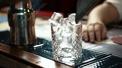 Close up of whisky glass being fulfilled with ice in stylish bar, slow motion.