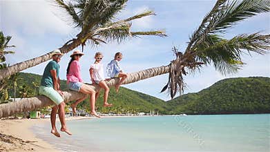 Young family on beach vacation on palm tree. Parents and kids having fun together on the coast of Caribbean on Antigua