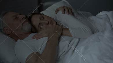 Elderly husband and wife sleeping in bed, woman put head on man chest, loving