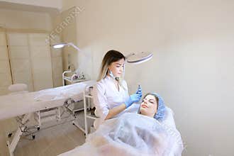 Lady at cosmetology cabinet getting tattooing eyebrows by cosmetologist.