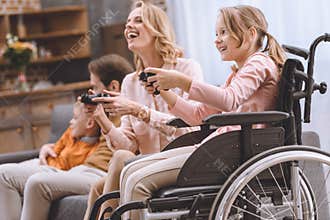 happy family with disabled child in wheelchair playing with joysticks together