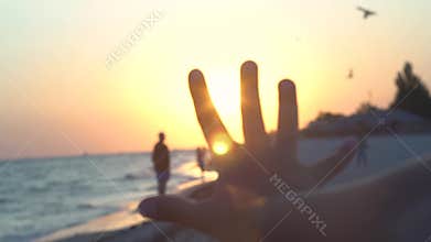 Child`s palm against the sunset on the coast