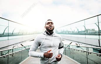 Young sporty black man runner running on the bridge outside in a city.