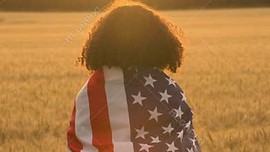 African American girl teenager female young woman holding an American USA Stars and Stripes flag in a wheat field at sunset or sun
