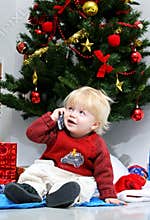 Young boy talking on mobile phone under a christmas tree.