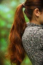 woman with long thick brown hair pony tale close up photo on green summer garden background