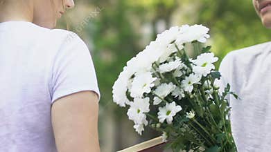 Closeup of teen boy giving flowers to girl, tender first love in adolescence