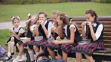 Girls College student wearing the same school uniform eating sandwiches sitting on a bench in the garden, laughing and