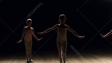 Three little girls dancers dance ballet on stage on a black background.