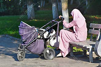Nevinnomyssk, Russia, September, 13, 2018. Muslim woman sitting on a bench and cradles a child in a wheelchair on the Boulevard of