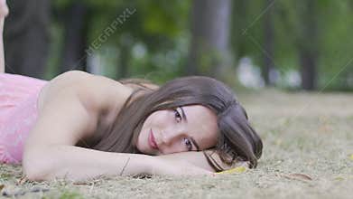 Relaxed beautiful lying woman opens eyes looks in camera, dolly shot outdoors