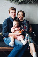 Parents and daughter sitting on sofa under big fir wreath.