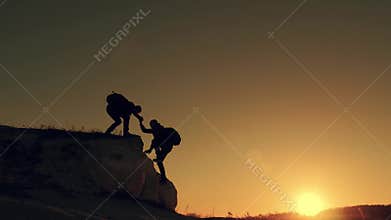 Silhouette of helping hand between two climber. two hikers on top of the mountain, a man helps a man to climb a sheer