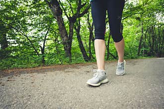 Close-up of a foot of a sporty girl in leggings and sneakers before jogging in the forest. The concept of outdoor sports