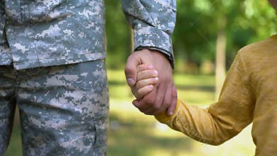 Serviceman holding boys hand, army defending safe future, family togetherness