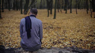 Young man sitting alone in autumn park, feels depression, nostalgia, loneliness