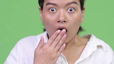 Young beautiful Asian woman looking shocked while covering mouth
