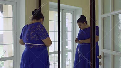 Fat girl in a blue dress in front of a mirror
