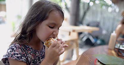 Cute little girl at wooden table eating burrito with blurry background