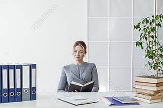 a business woman in a suit sits at an office desk with books