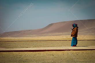 Peruvian woman in traditional clothing looks to cellphone, standing on a dry mountainous area