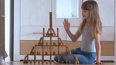Happy child girl playing game stacking wooden toy blocks in high pile structure. Hand movement control and building