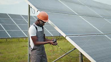 Professional african engineer in helmet and uniform using multimeter for measuring amperage in solar panels. Concept of