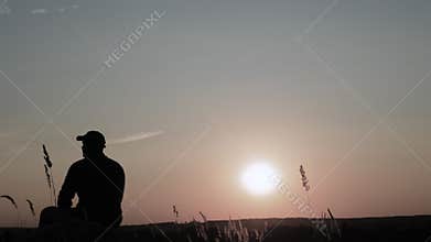 Silhouette is a sad guy. A lonely young man sits on a mountain at sunset. Pensive guy. The person is dreamy