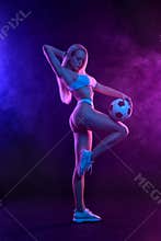 Sexy fitness and sport concept. Fit woman in the neon lights with soccer ball.