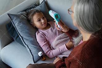 Grandmother taking care of her ill grandchild lying on sofa