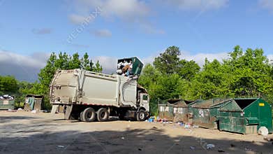 A Waste Trash truck dumping a dumpster over the top at a county dump