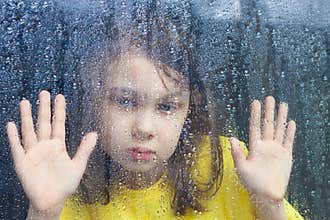 a little girl behind a rain-splattered window