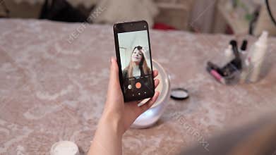 blogger young woman filming daily make-up tutorial the smartphone. girl live streaming cosmetics product review in home