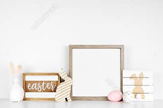 Mock up square wood frame with shabby chic Easter decor on a white shelf against a white wall