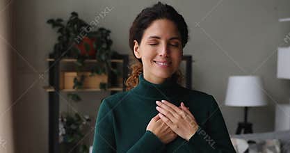 Beautiful sincere woman standing indoor put folded palms on heart