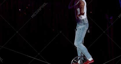 Circus performer is balancing on a unicycle on a rope, show on stage, 4k