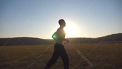 Young muscular man running through field with beautiful landscape at background. Male athlete trains in nature. Soldier