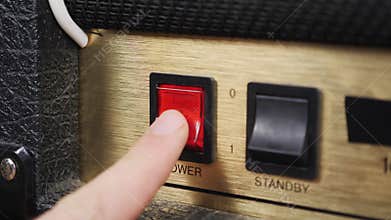 Male hand is turning switch of guitar amplifier on. Turn on power switch button on vintage guitar amplifier. Music concept. Sound