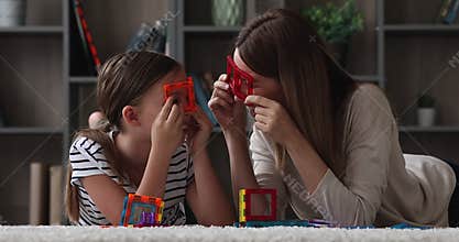 Cheery mom and daughter having fun fooling with magnetic constructor