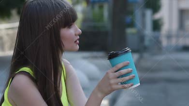 Bemused young girl drinks a cup of tea on street