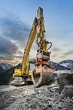 huge clamshell grab excavator for natural stone masonry in front of alp mountains