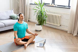Home workout and healthy lifestyle concept - man meditates at home - using from the internet to monitor the workout. He